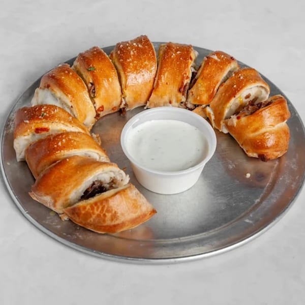 A ring of golden-brown, sliced stromboli or calzone pieces with a side of white dipping sauce.