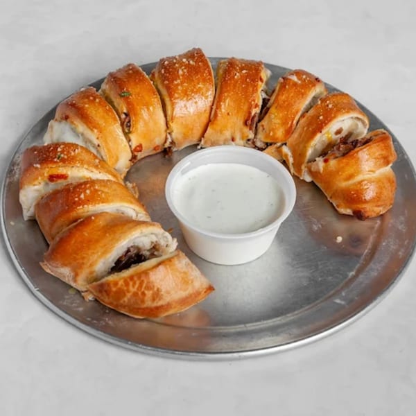 Sliced calzone arranged in a circle with a side of ranch dressing on a metal pizza pan.