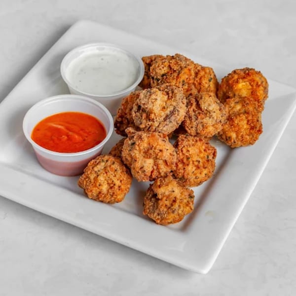 Crispy fried mushrooms with two dipping sauces, ranch and buffalo, on a white plate.