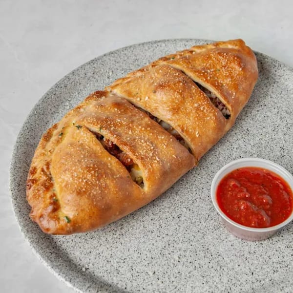 Golden-brown calzone with visible fillings and a side of red marinara sauce on a speckled gray plate.